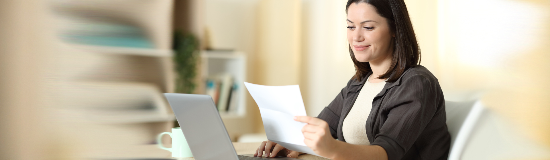 woman holding and viewing bill while using her laptop